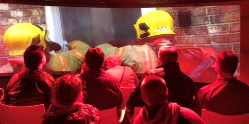 Image of visitors in our theatre watching fire fightrs enter a burning building.